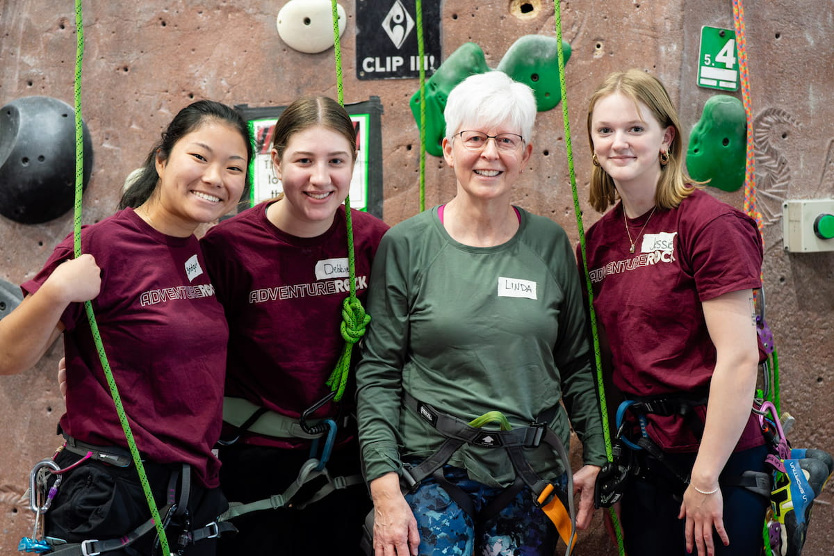 Four women standing in front of a rock climbing wall at a climbing gym