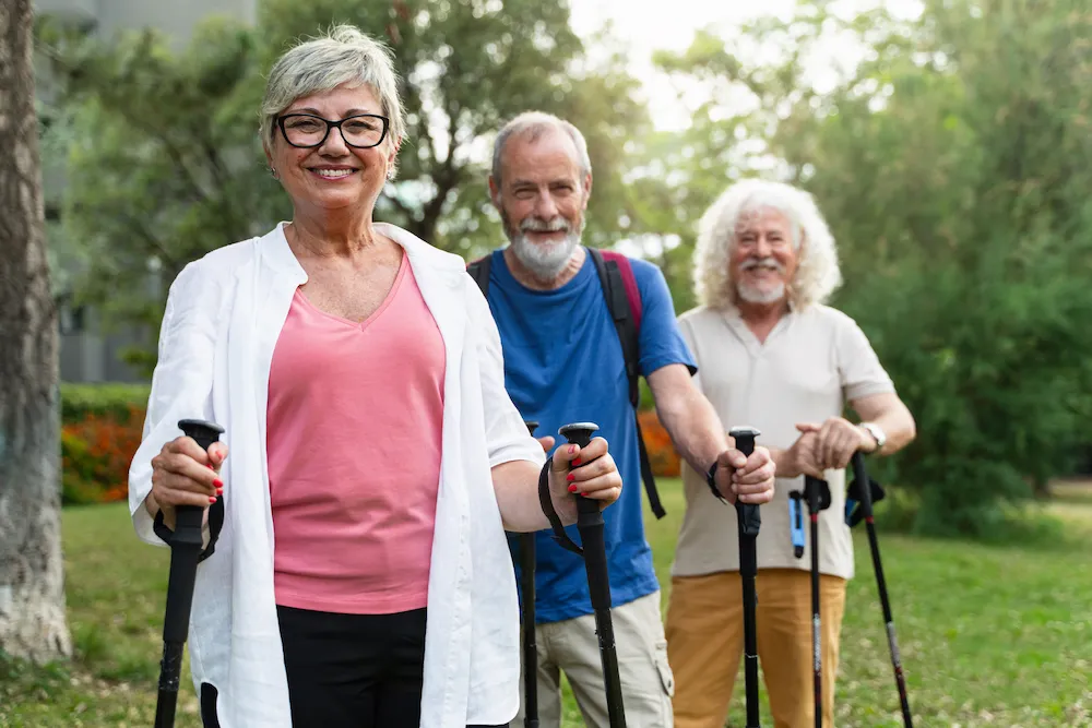 Three smiling people hiking using hiking poles.